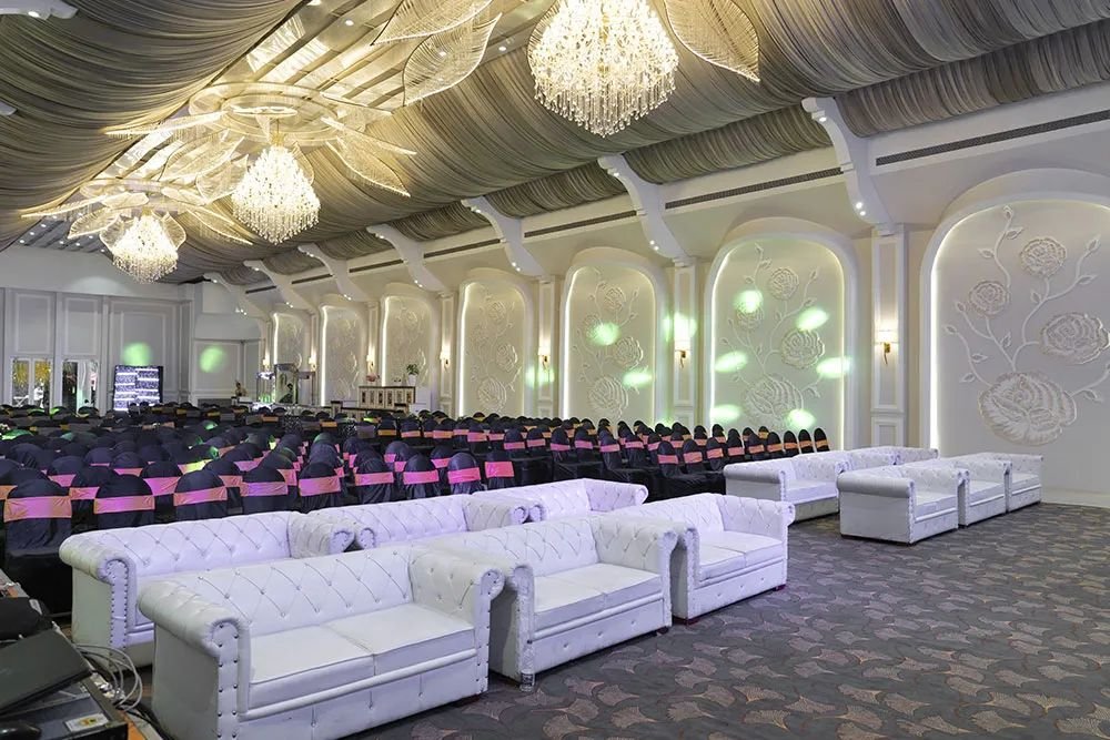 The hall with chandeliers, rows of chairs facing the stage and white lounge sofas at the front