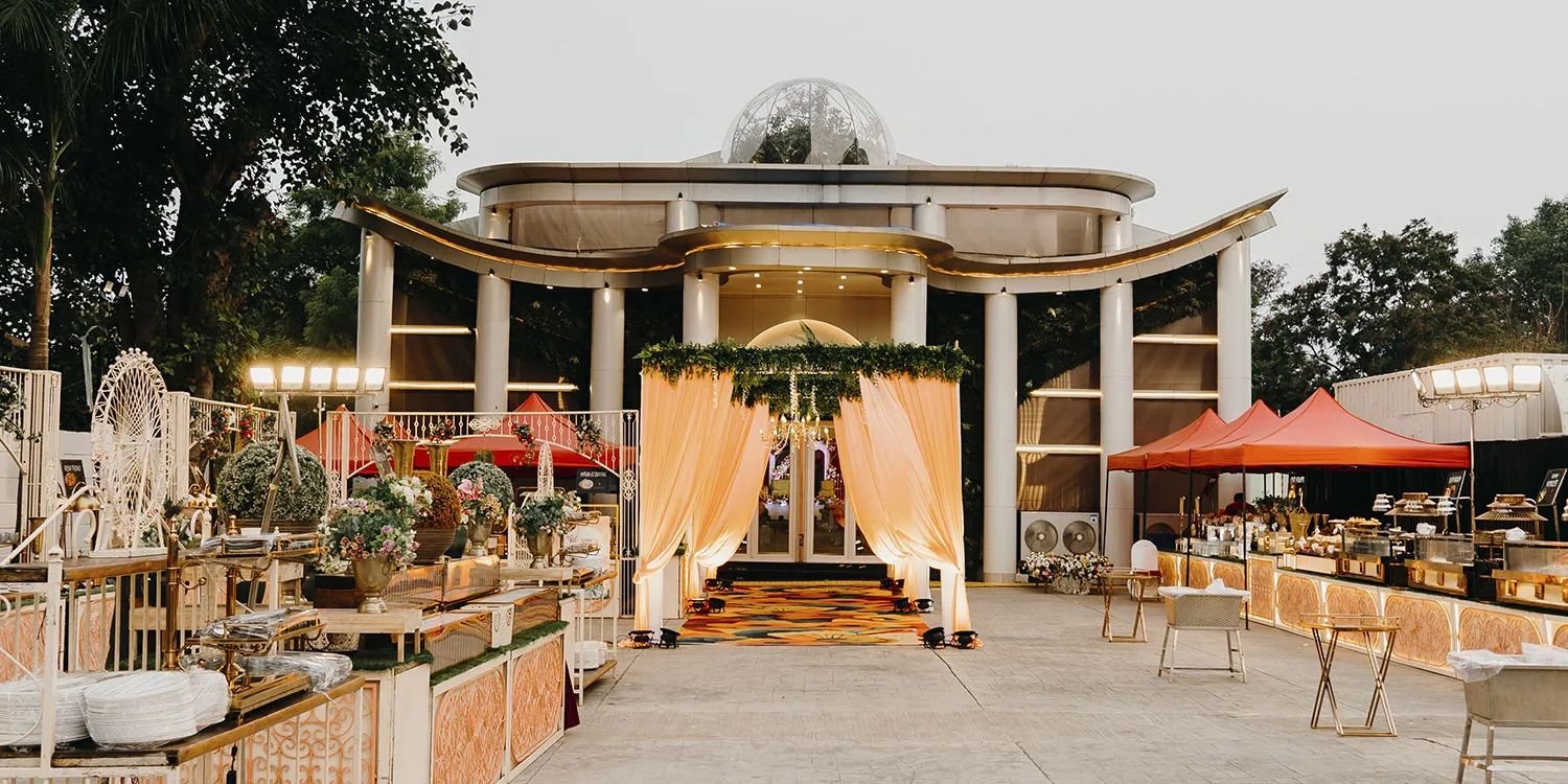 The domed pavilion at dusk with a peach-draped entrance, serving counters and orange-red canopies on the lawn